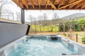Ein Whirlpool unter einem hölzernen Dach, umgeben von einer grünen Landschaft und Bäumen.