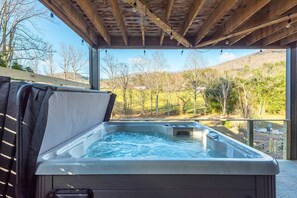 Ein Whirlpool unter einer Holzpergola mit Blick auf eine grüne Landschaft.