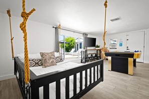A room with a four-poster bed, a desk with a foosball table, and a large window with a view of greenery. - The Cabana Cove Cabana Bar Pool Game Room (Scottsdale)