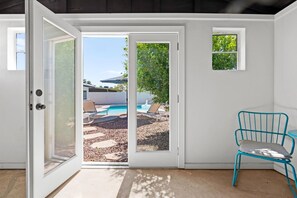 A room with a sliding glass door leading to an outdoor area with a pool, lounge chairs, and a blue chair. - The Cabana Cove Cabana Bar Pool Game Room (Scottsdale)