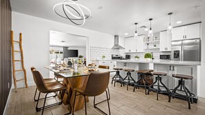 A modern kitchen with a central island, bar stools, and a dining area with chairs. - The Cabana Cove Cabana Bar Pool Game Room (Scottsdale)