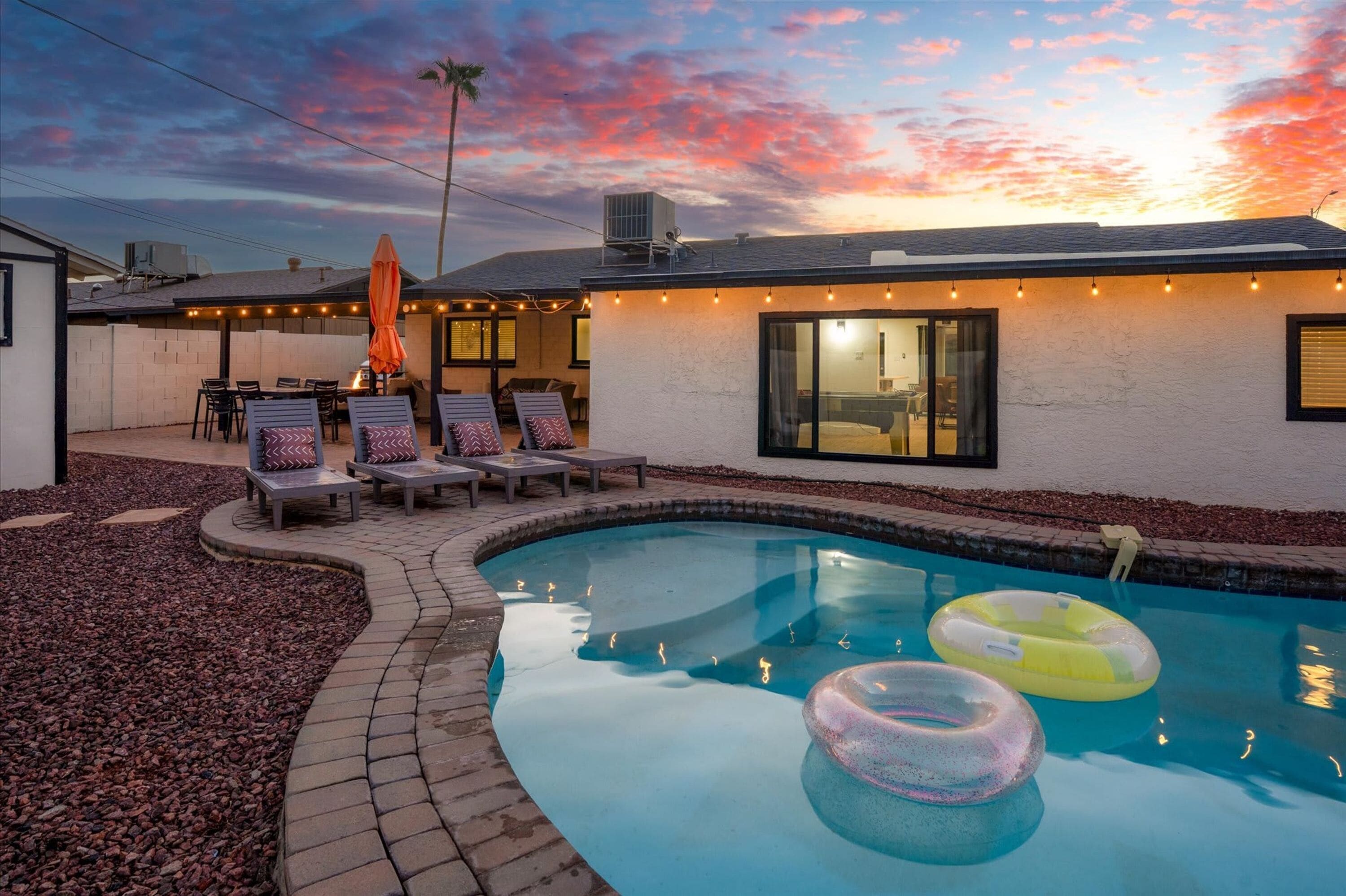 A backyard with a swimming pool, lounge chairs, and a patio area.
