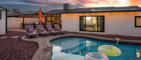 A backyard with a swimming pool, lounge chairs, and a patio area.