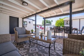 A covered patio area with wicker furniture, a table, and a potted plant. - The Cabana Cove Cabana Bar Pool Game Room (Scottsdale)