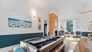 A pool table in a room with a view of the sea, a fireplace, and a seating area with a sofa and chairs. - Burkes Beach Reserve Golf Sim Pickleball Sleeps 24 (Hilton Head Island)