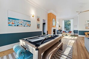 A pool table in a room with a view of the sea, a fireplace, and a seating area with a sofa and chairs. - Burkes Beach Reserve Golf Sim Pickleball Sleeps 24 (Hilton Head Island)
