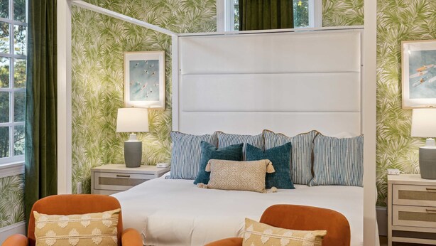 A four-poster bed with multiple pillows, two nightstands with lamps, and a window with curtains. - Burkes Beach Reserve Golf Sim Pickleball Sleeps 24 (Hilton Head Island)