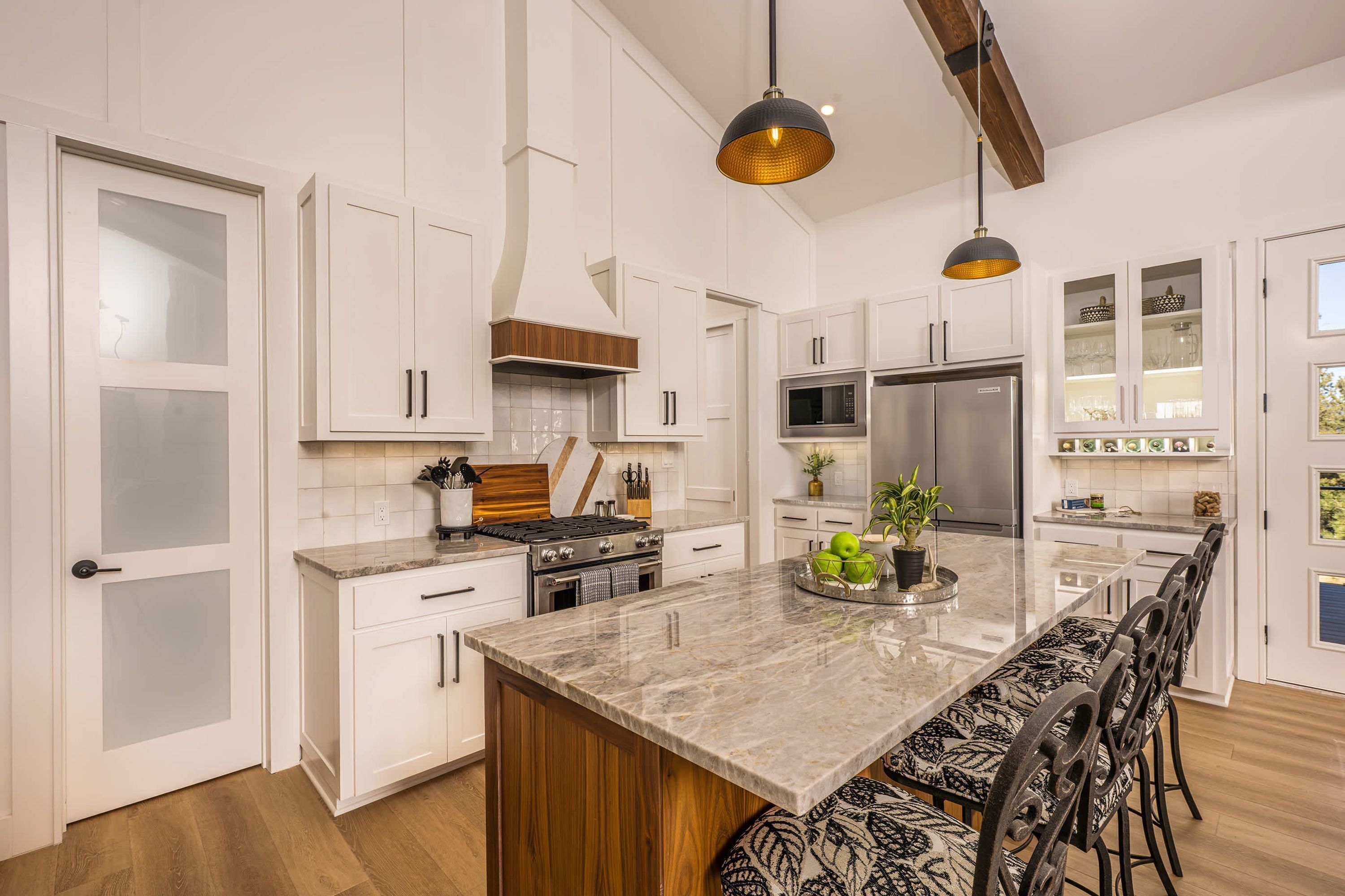Cocina moderna con armarios blancos, una isla central con asientos, electrodomésticos de acero inoxidable e iluminación colgante.