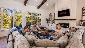 A modern living room with a fireplace, a large window, and a Netflix sign. - The Pines of Valle Grande Hot Tub Fireplace (Angel Fire)