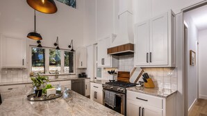 A modern kitchen with white cabinetry, a marble countertop, and a large island. - The Pines of Valle Grande Hot Tub Fireplace (Angel Fire)