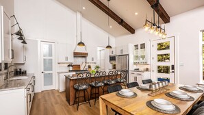 A spacious kitchen with white cabinetry, a wooden dining table, and a built-in island with bar stools. - The Pines of Valle Grande Hot Tub Fireplace (Angel Fire)