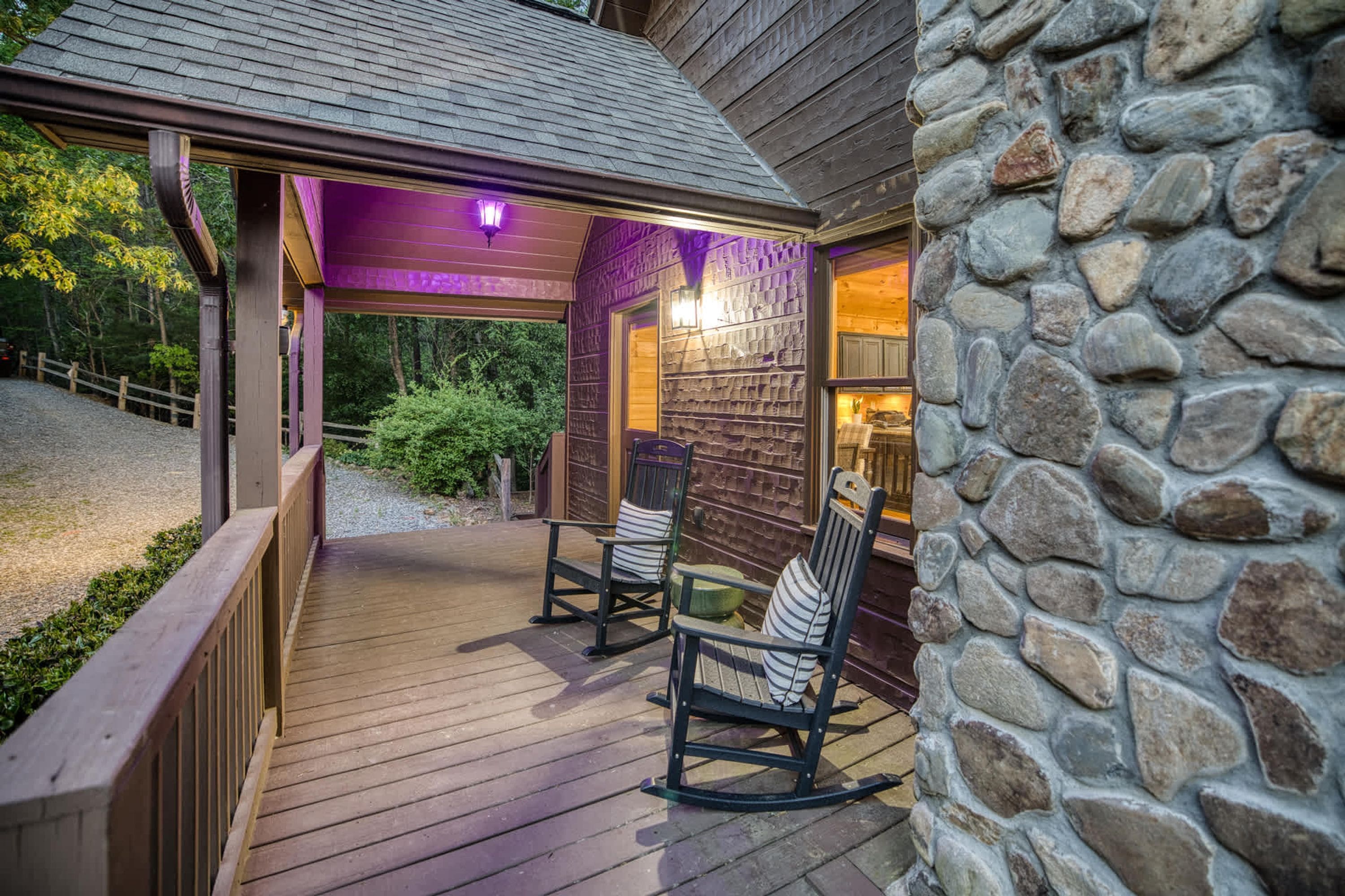 A wooden deck with two rocking chairs and a stone wall.