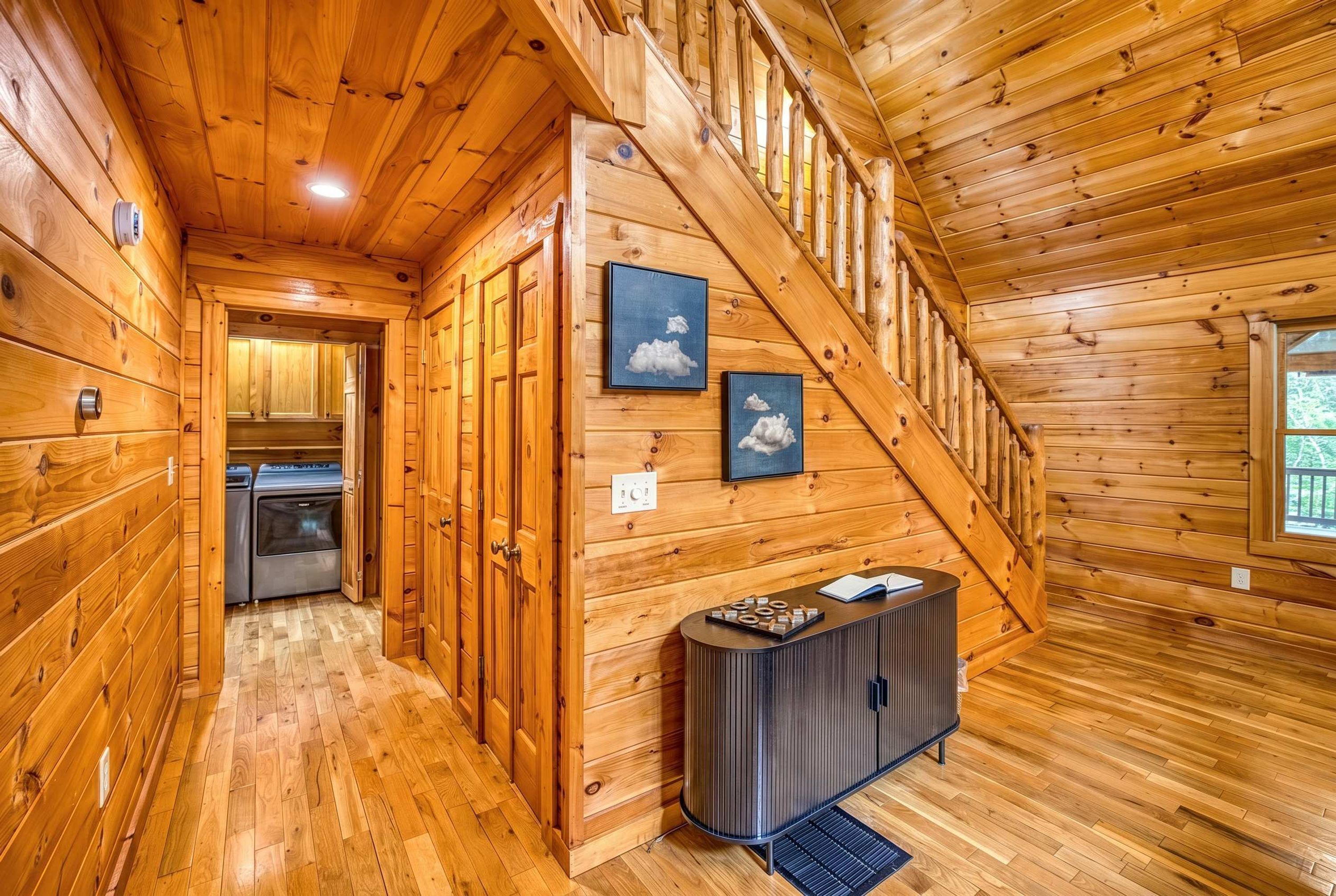 Un intérieur en bois comprenant un escalier, un coin cuisine et un couloir menant à une porte.