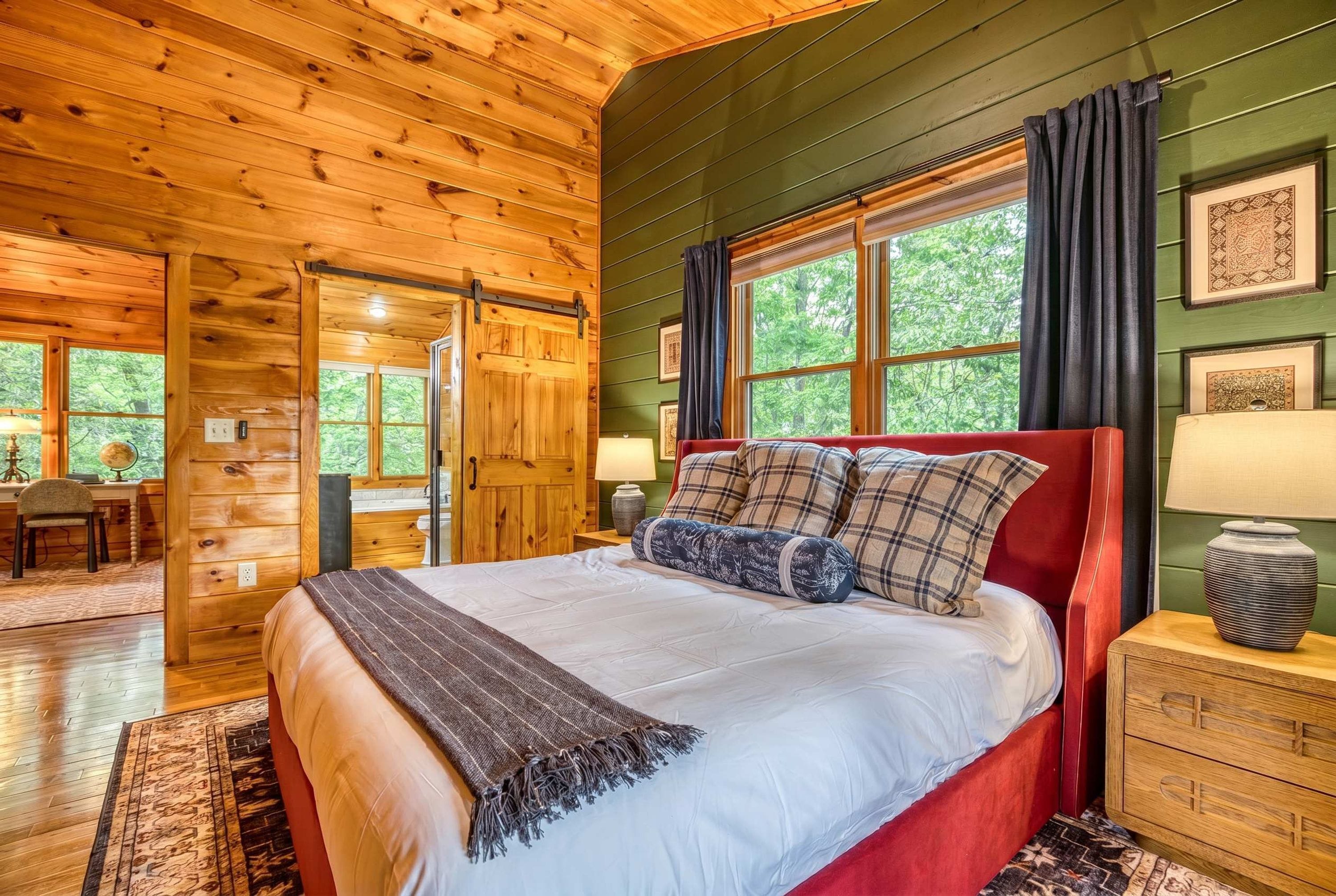 A wooden cabin bedroom with a bed, a nightstand, a dresser, and a window with curtains.