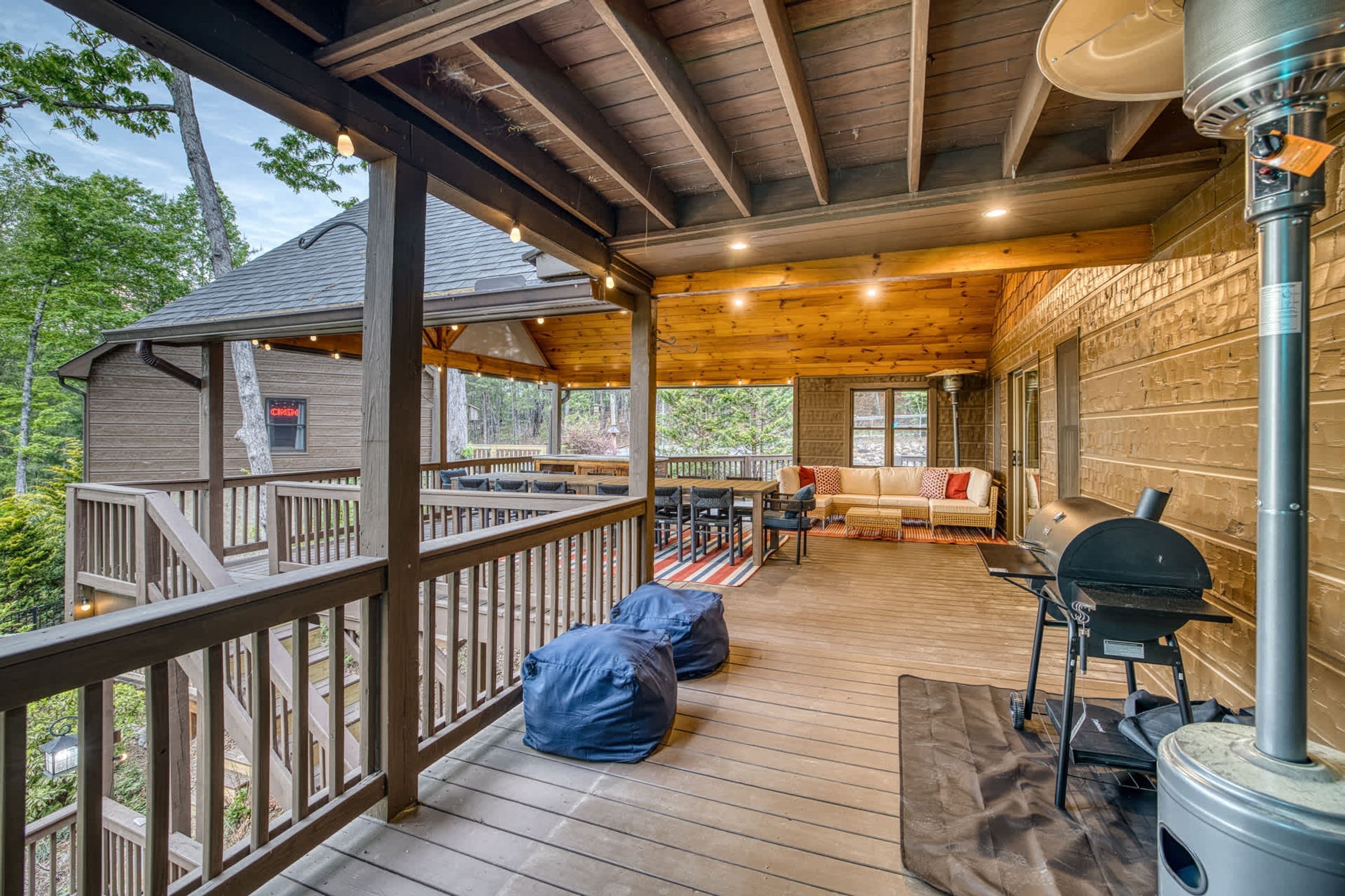 A covered deck with a wooden floor, a barbecue grill, and a seating area with a sofa and chairs.