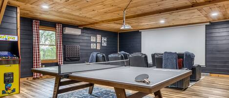 Ein Tischtennis-Tisch in einem Raum mit Holzboden, einer Projektionsleinwand und einer Spielkonsole.