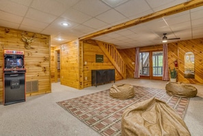 A log cabin interior with a gaming machine, a fireplace, a staircase, and a large rug. - Heated Pool Mtn Views Sleeps 20 Game Room (Morganton)