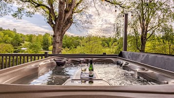 A hot tub with a bottle of wine and glasses, surrounded by trees and a view of the landscape.