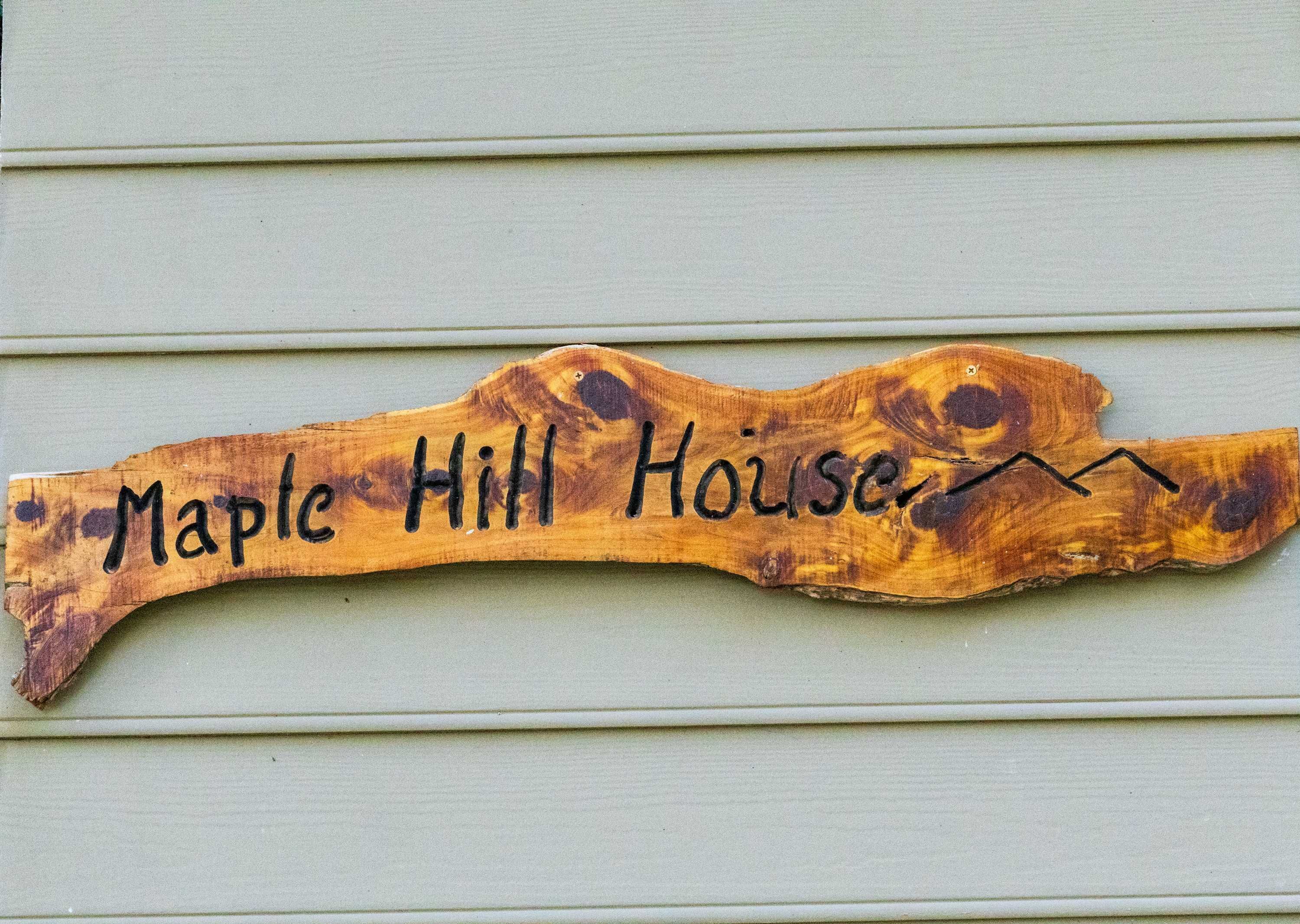 Uma placa de madeira com o texto 'Maple Hill House' fixada em um edifício.