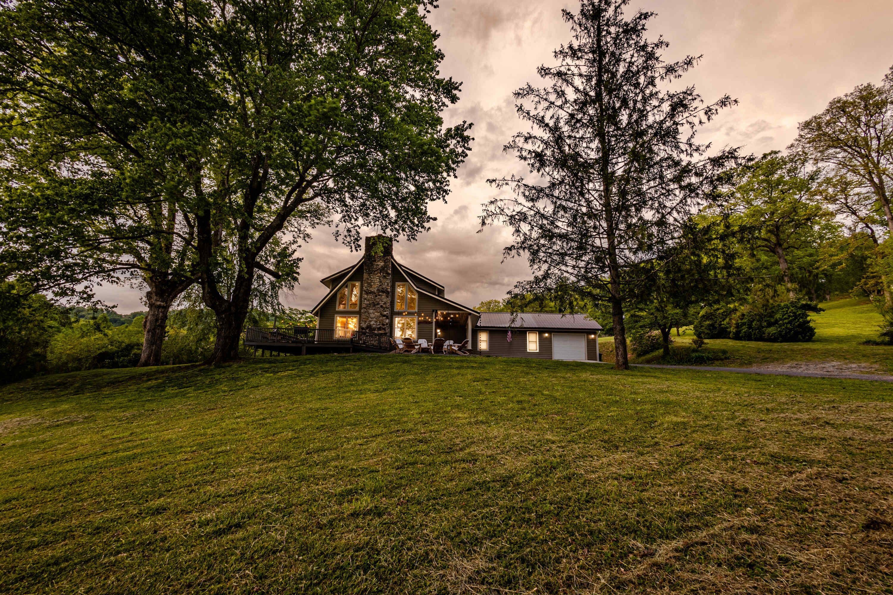 A house with a stone chimney, surrounded by trees and a grassy yard.