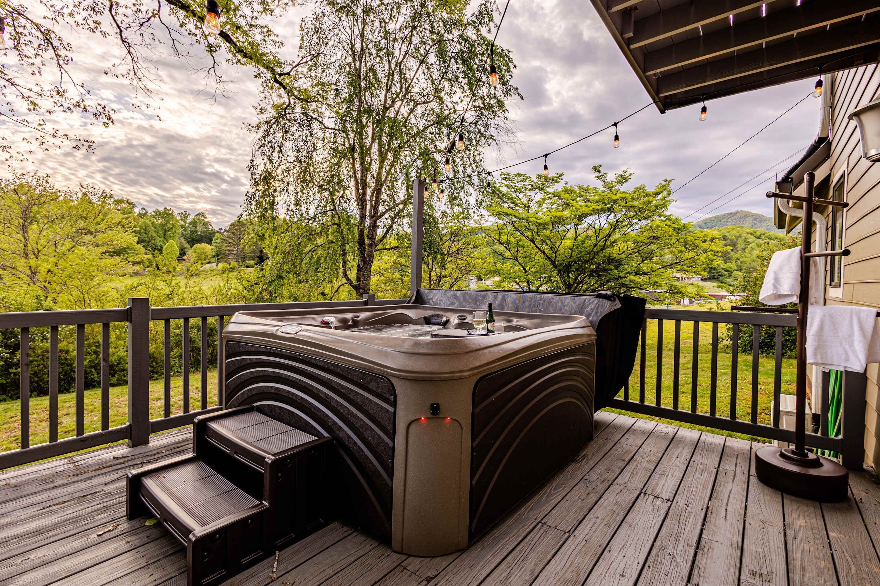 A hot tub on a wooden deck with a view of a green landscape and a house in the background.