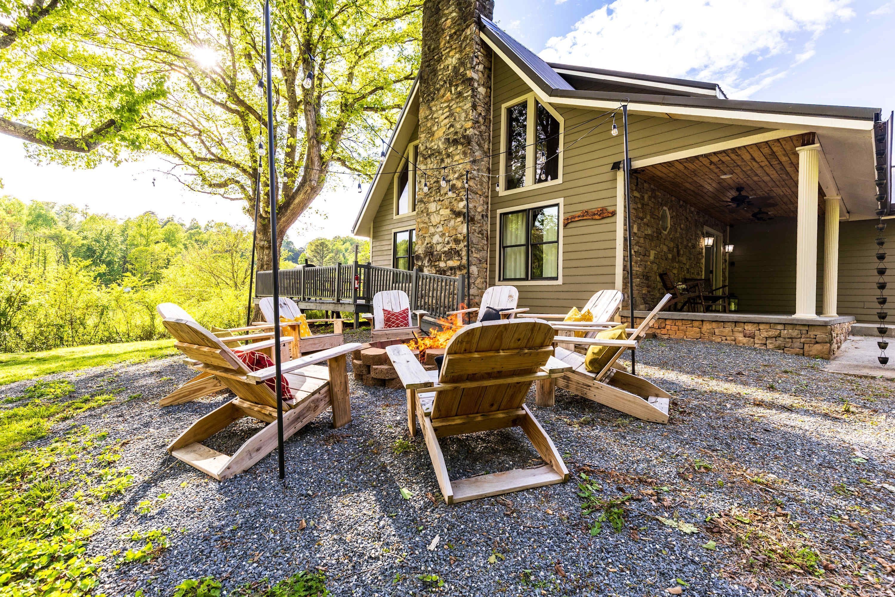 A cozy outdoor seating area with Adirondack chairs and a fire pit, surrounded by a stone wall and a wooden deck.