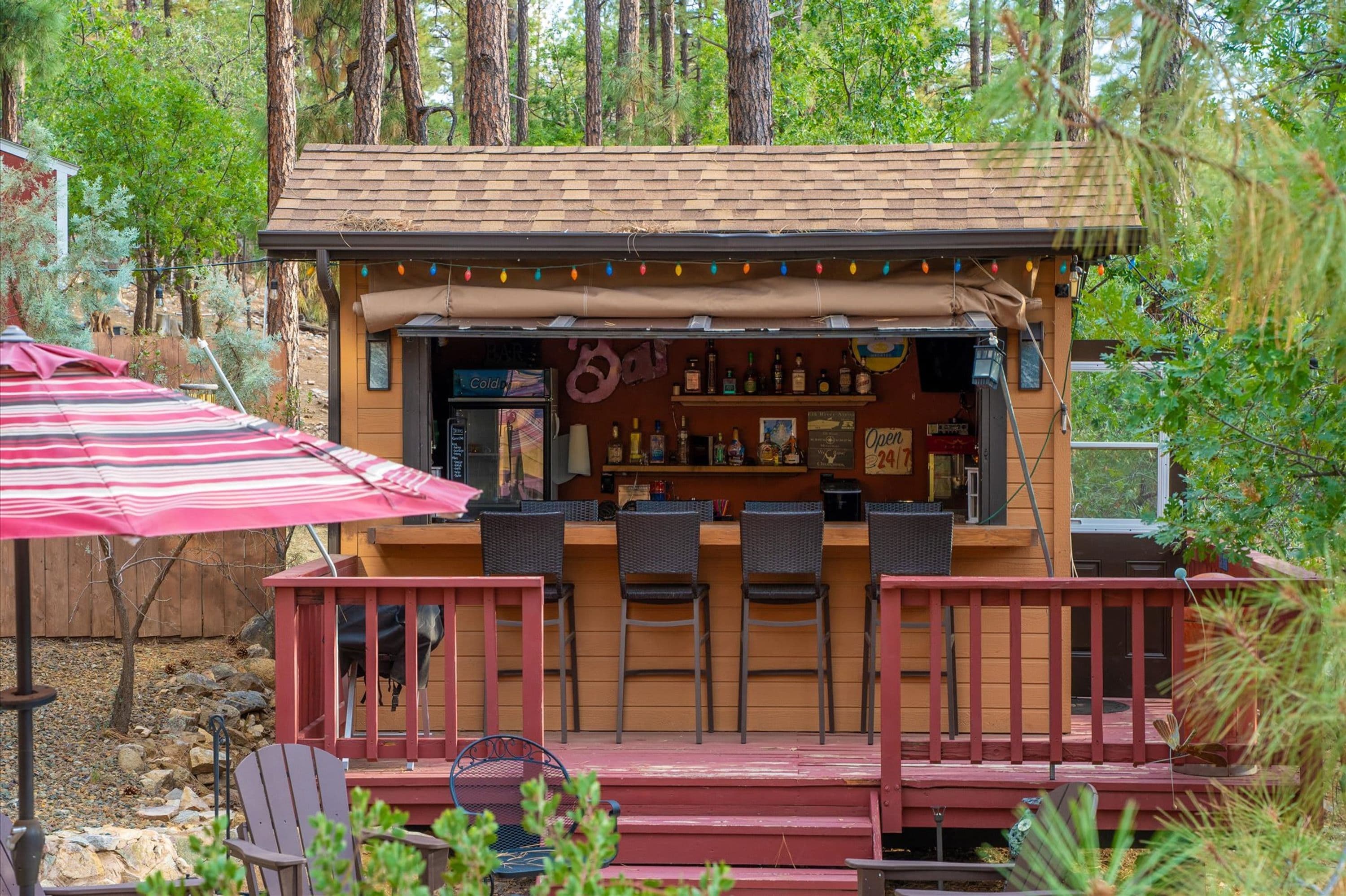 Un bar con terraza de madera, mesas al aire libre y una variedad de botellas en estanterías.