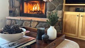 A cozy living room with a stone fireplace, a television, and a wooden coffee table with decorative items. - Wildlife Views Hot Tub Fire Pit Games (Prescott)