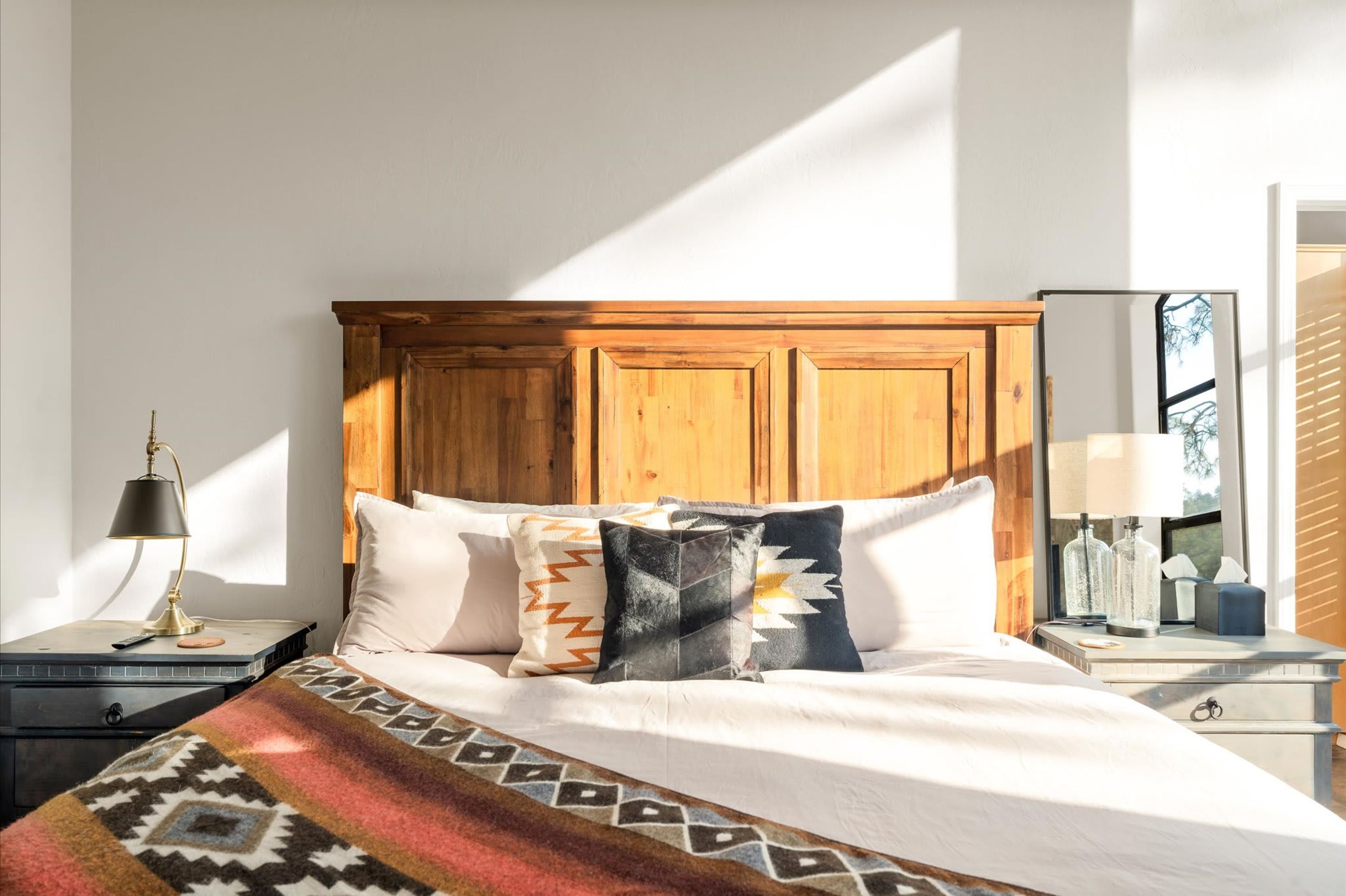 A bed with a wooden headboard, a patterned throw blanket, and multiple pillows.