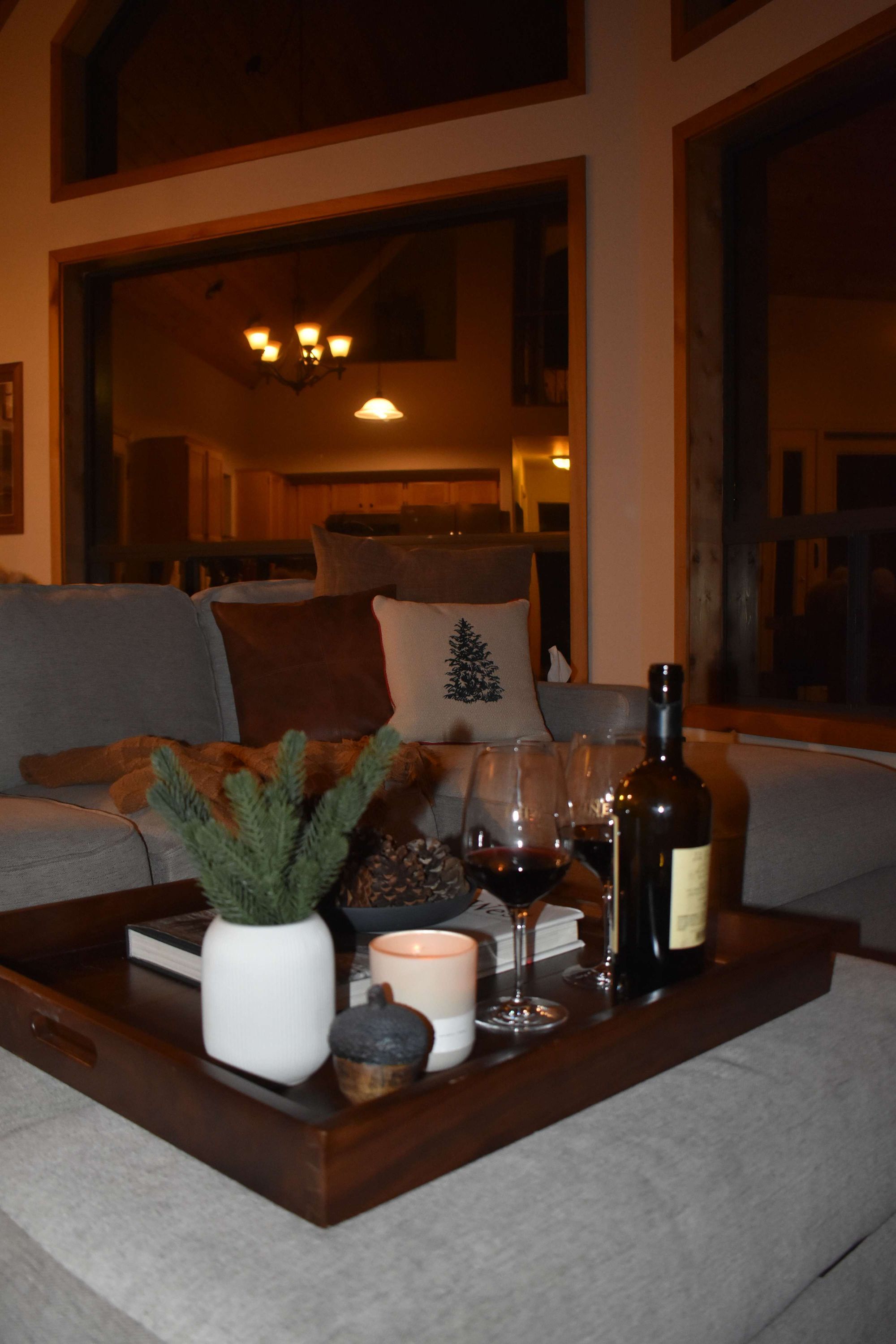 A cozy living room with a wooden coffee table holding a candle, a bottle, and glasses.