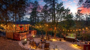 A cozy outdoor patio with a fire pit, seating, and a bar area, surrounded by trees. - Wildlife Views Hot Tub Fire Pit Games (Prescott)