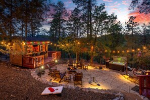 A cozy outdoor patio with a fire pit, seating, and a bar area, surrounded by trees. - Wildlife Views Hot Tub Fire Pit Games (Prescott)
