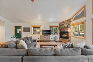 Una sala de estar moderna con un sofá seccional, un televisor de pantalla plana, una chimenea y ventanas amplias.
