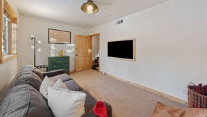 Una sala moderna con un sofá, un aparador verde, un televisor montado y una puerta de madera que da a otra habitación.