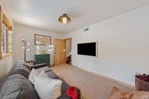 Uma sala de estar moderna com um sofá, um aparador verde, uma televisão montada e uma porta de madeira que dá para outro cômodo.