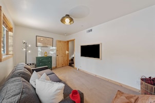 Una sala moderna con un sofá, un aparador verde, un televisor montado y una puerta de madera que da a otra habitación.
