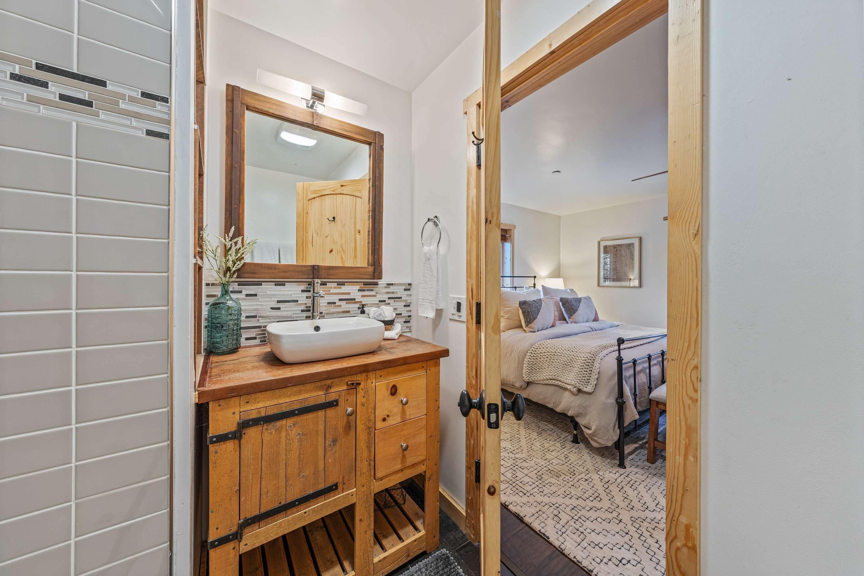 Un baño con tocador de madera, un espejo grande y salpicadero de azulejos.