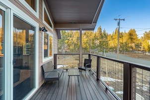 Una terraza de madera con dos sillas y una mesa, con vista a un área boscosa.