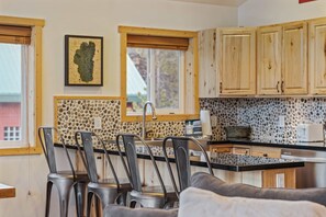 Uma cozinha com painel de backsplash de pedra, armários de madeira e um espaço de refeições com cadeiras de metal.