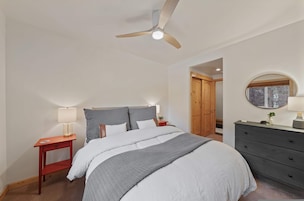 Un dormitorio con cama, mesitas de noche, cómoda, ventilador de techo y ventana con vistas.