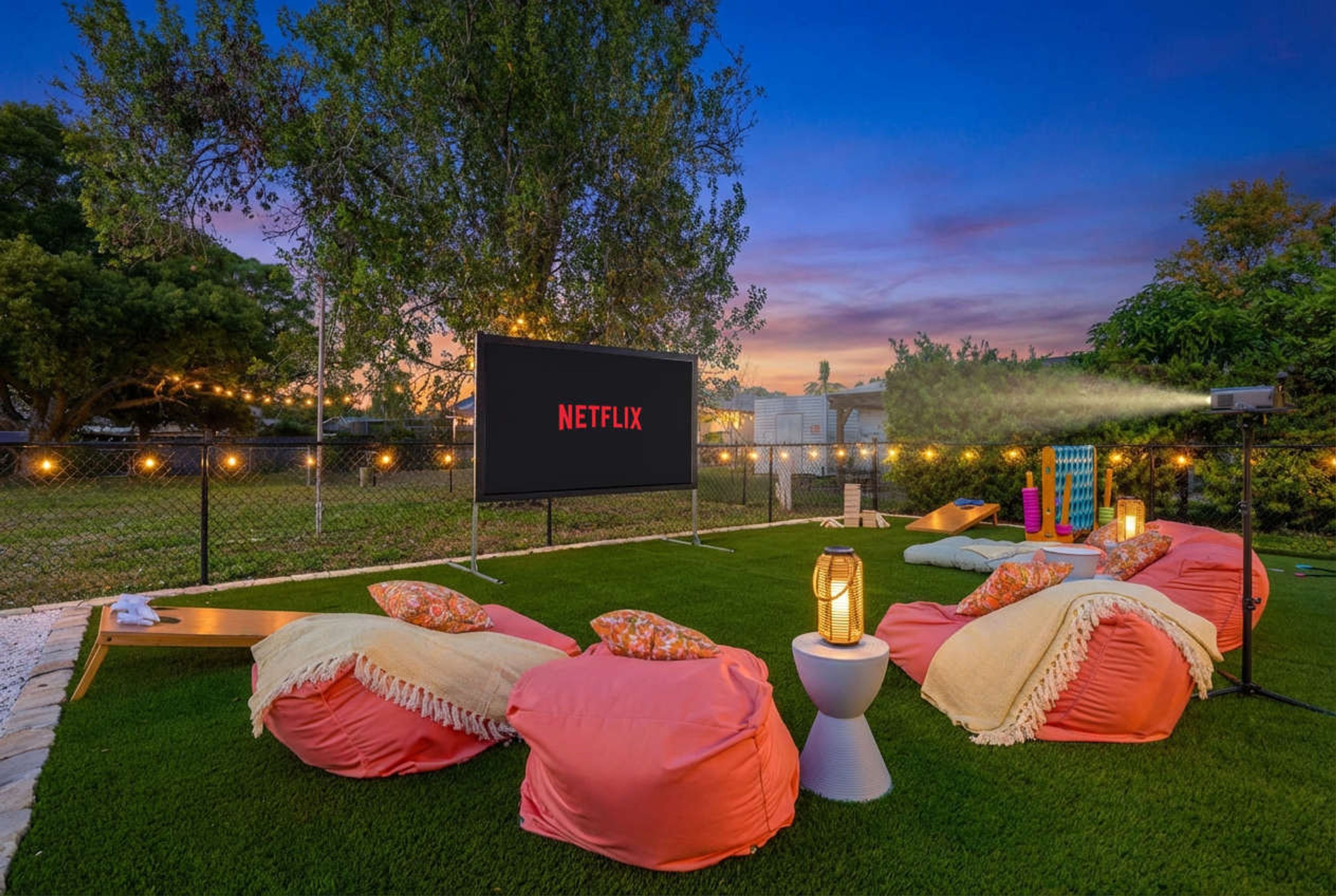 An outdoor seating area with a large screen displaying 'NETFLIX' and a grassy lawn.