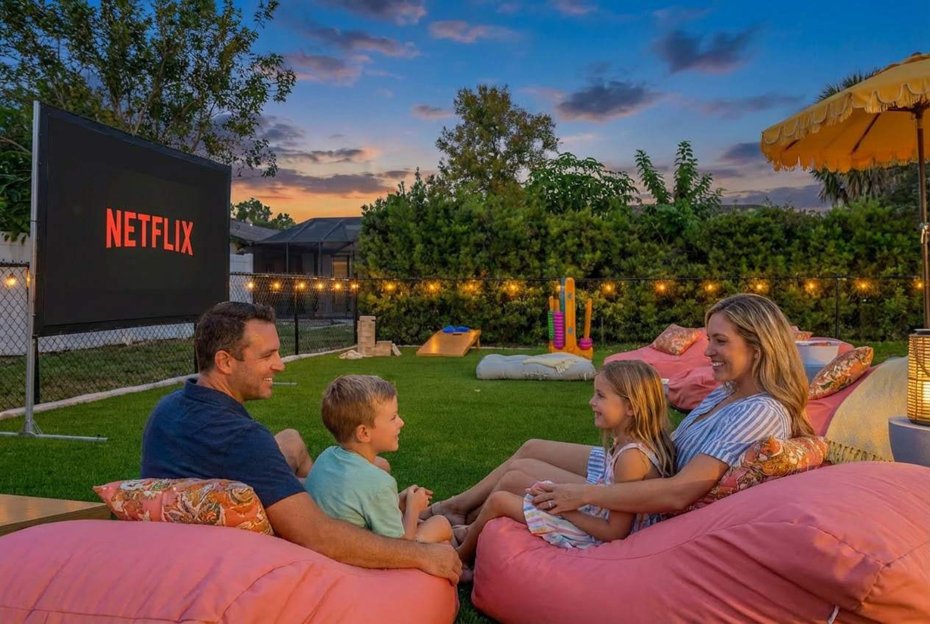 A family sitting on outdoor bean bags with a large screen displaying the Netflix logo.