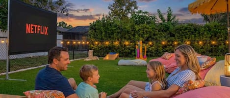 A family sitting on outdoor bean bags with a large screen displaying the Netflix logo.