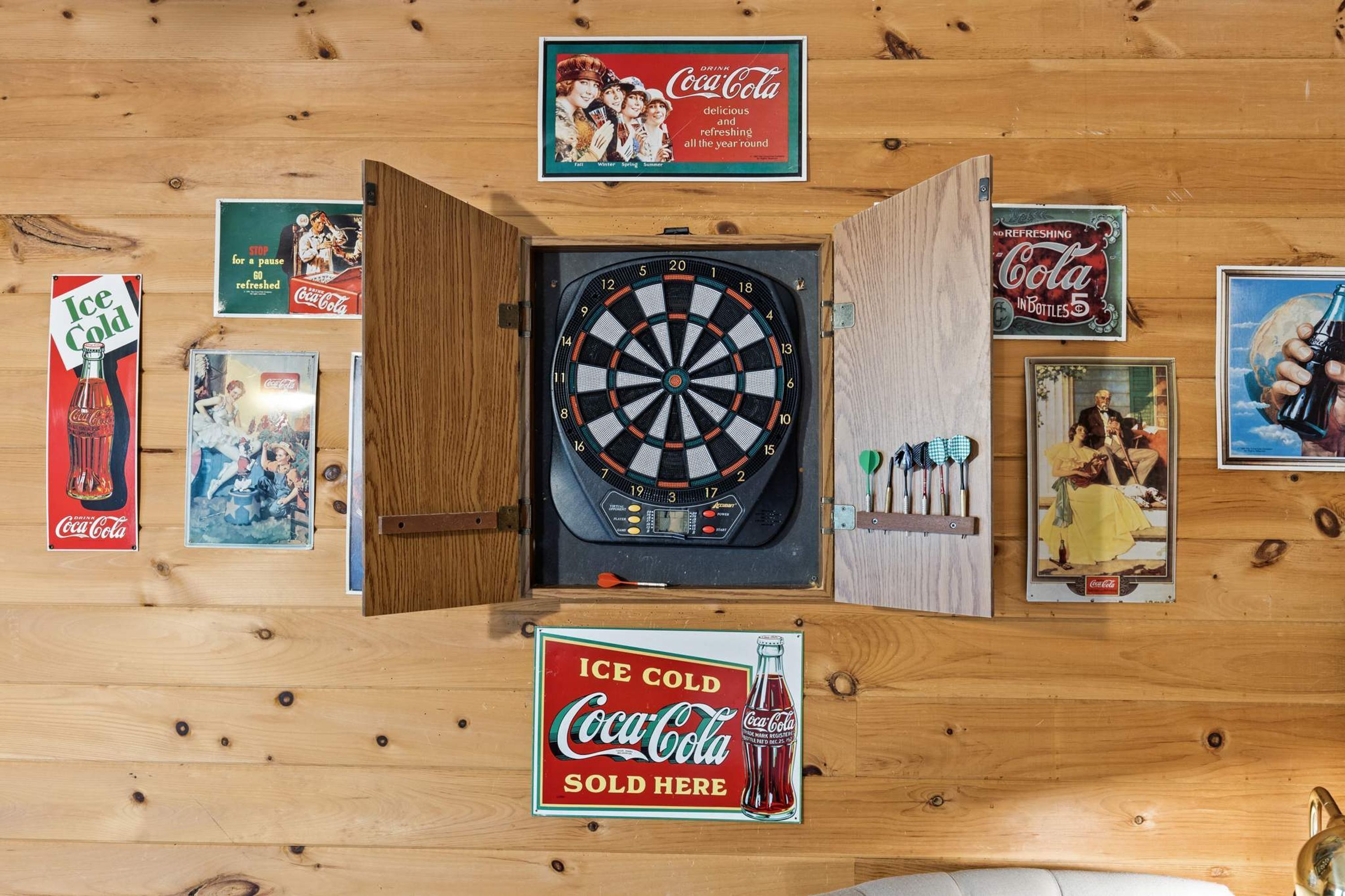 Eine Dartscheibe, umgeben von Werbeanzeigen für Coca-Cola im Vintage-Stil.