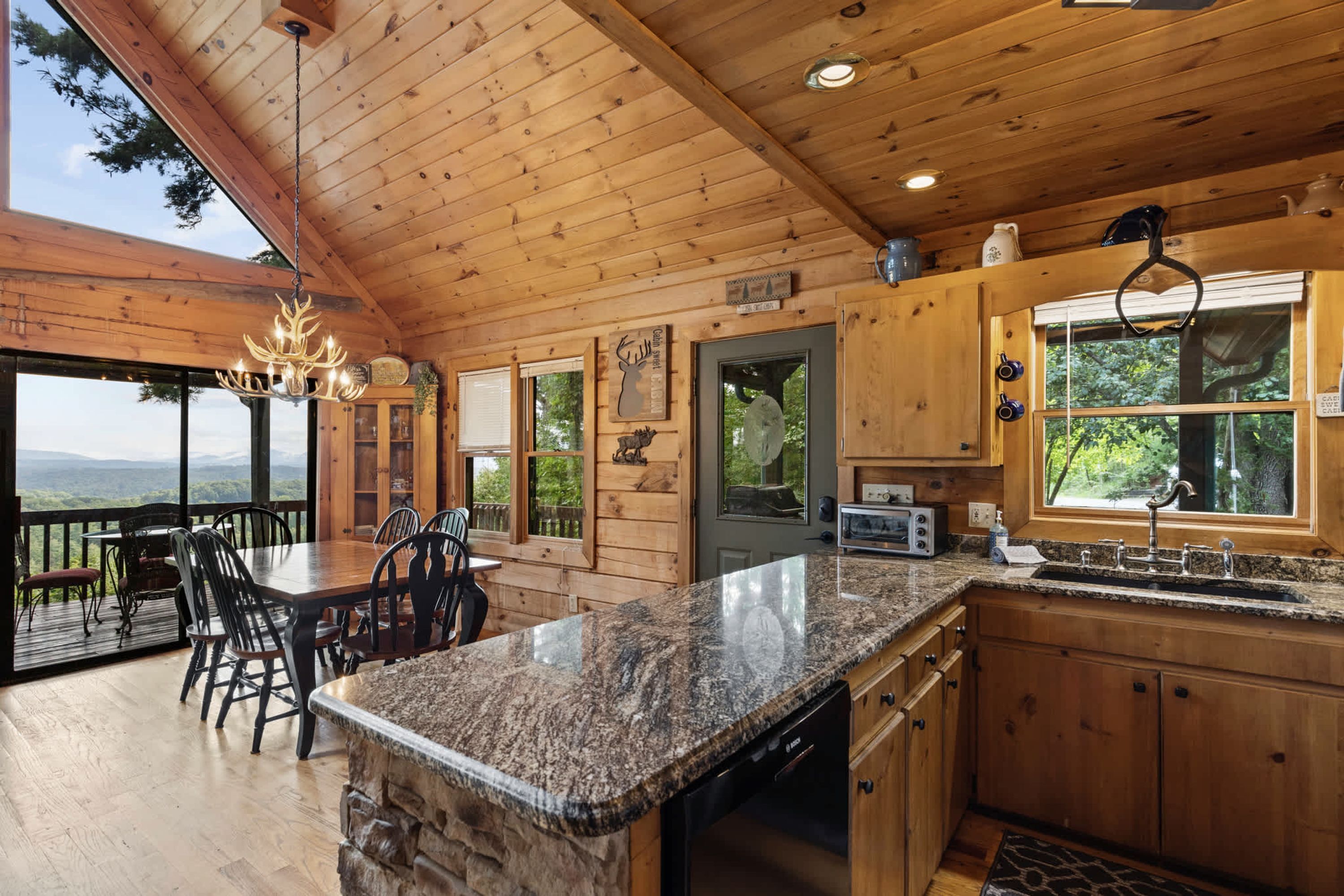 A cabin interior with a dining area, kitchen, and a large window offering a view.