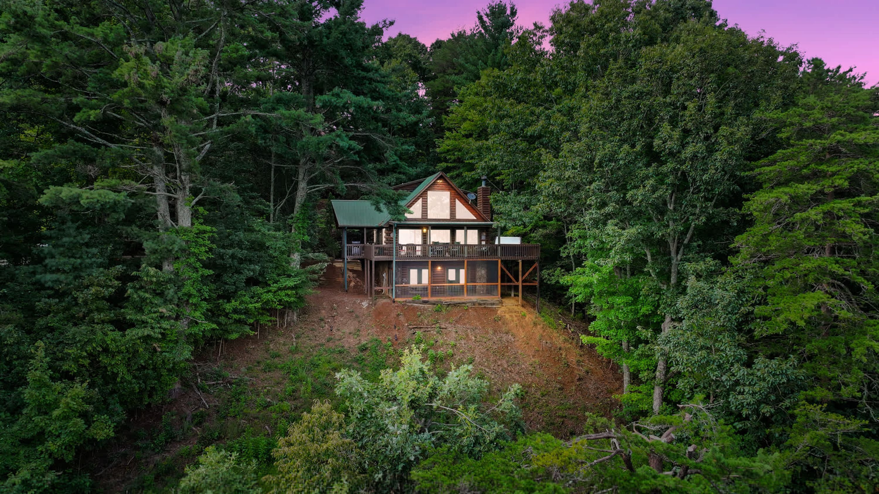 A cabin surrounded by dense forest, with a deck and a covered porch.