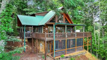 A cabin with a green roof, wooden deck, and a glass enclosure.