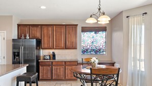 A kitchen with wooden cabinets, a stainless steel refrigerator, a built-in oven, a window with a stained glass design, and a dining area with a table and chairs. - Sleeps 14 Pool Spa Fire Pit Billiards EV Plug (Mesa)