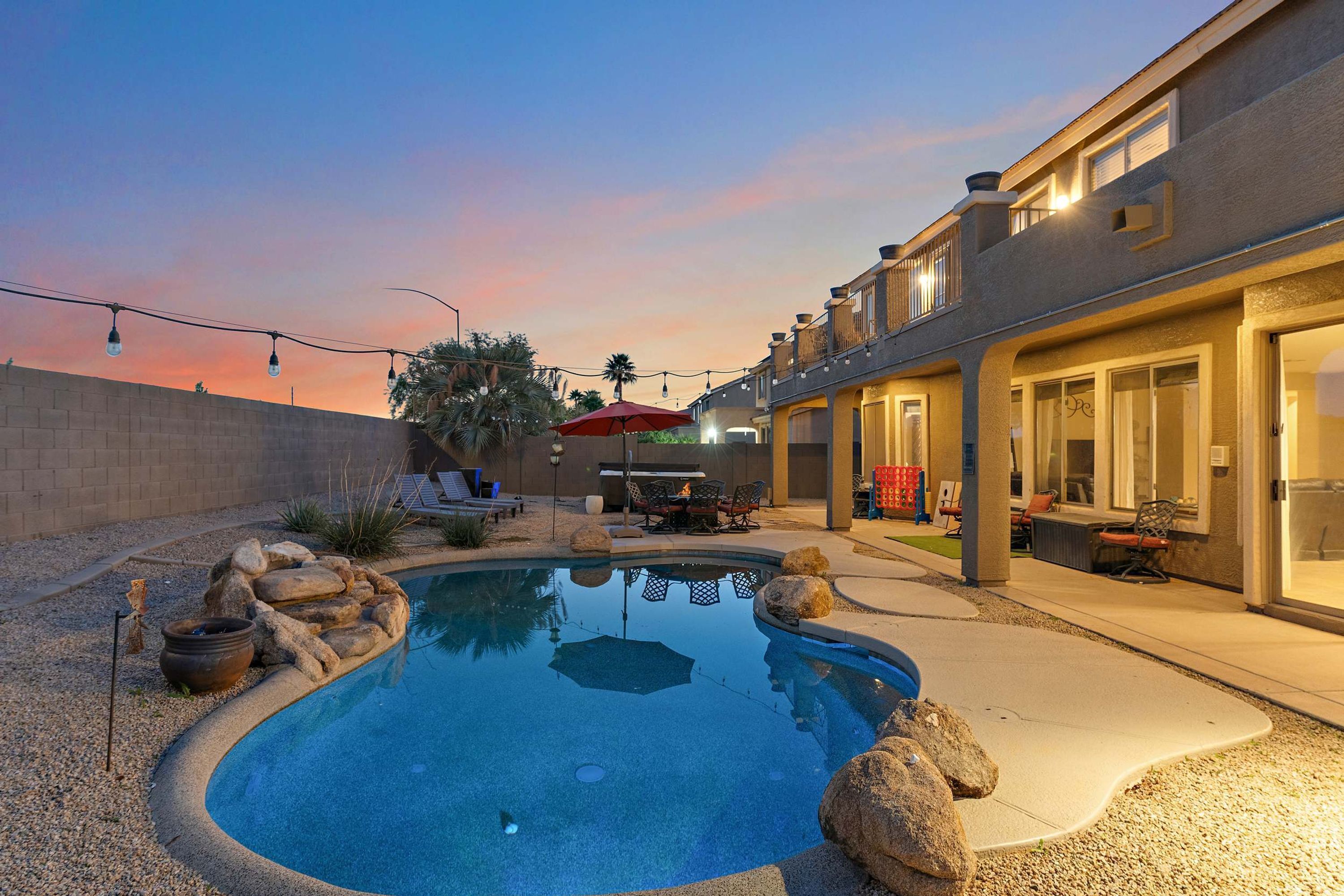 A swimming pool with a stone border, outdoor furniture, and a building with large windows.