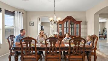 A dining room with a large wooden table, ornate chairs, a chandelier, and a large mirror.